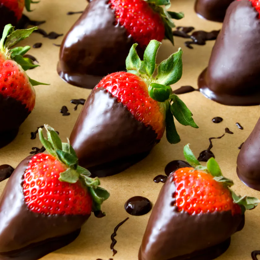 Several chocolate-dipped strawberries, aligned on baking paper.